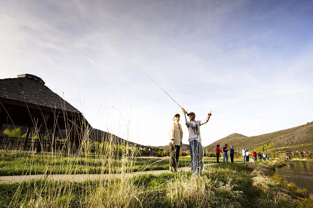 Two people fishing by a lake with a scenic background