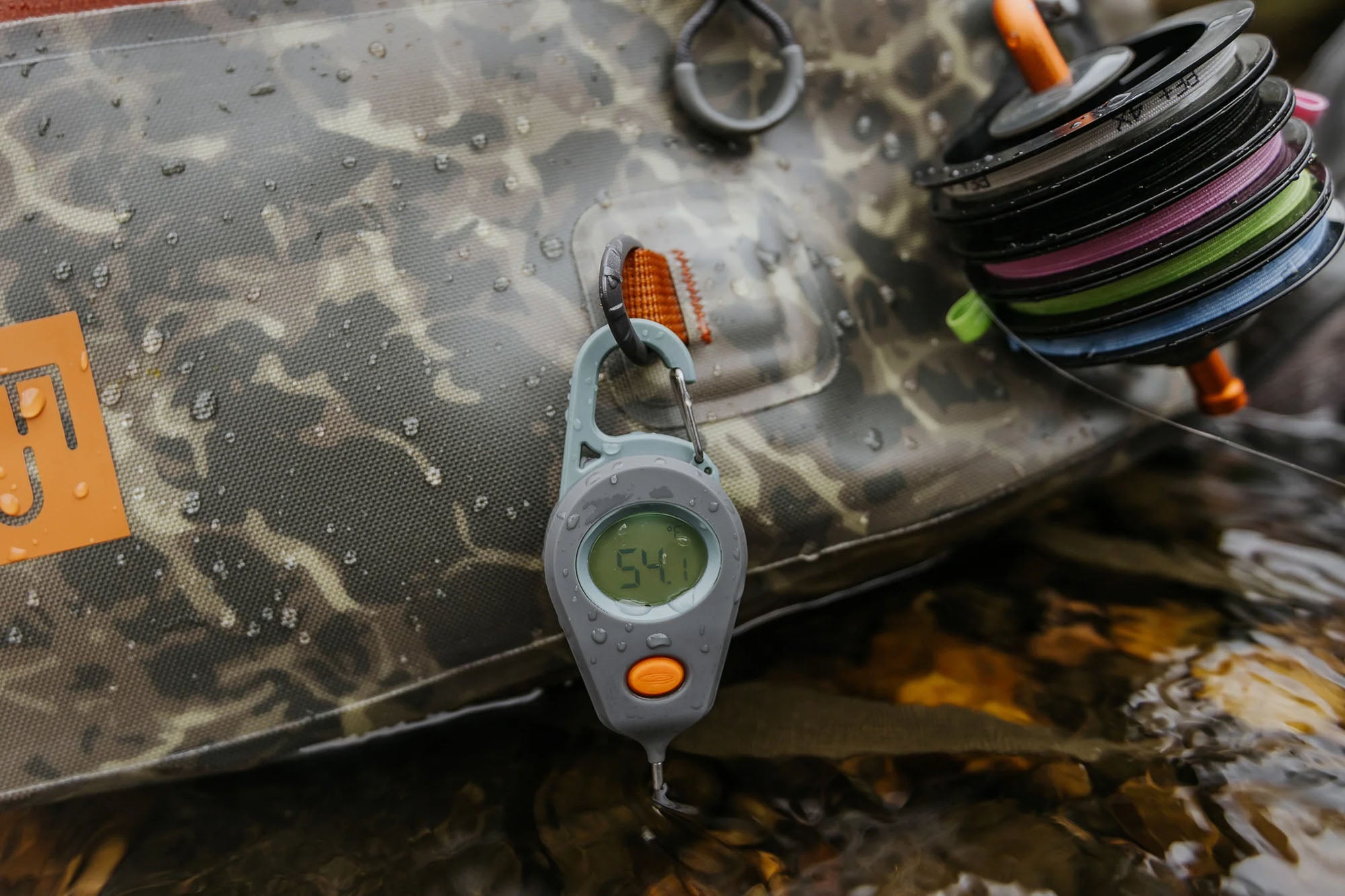 A digitial fishing thermometer from Fishpond  on a camouflage surface with fishing line spools.